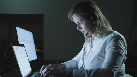 Woman-in-headset-working-with-laptop-in-dark-office